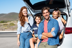 family of 4 smiling at camera on vacation, sitting in a car